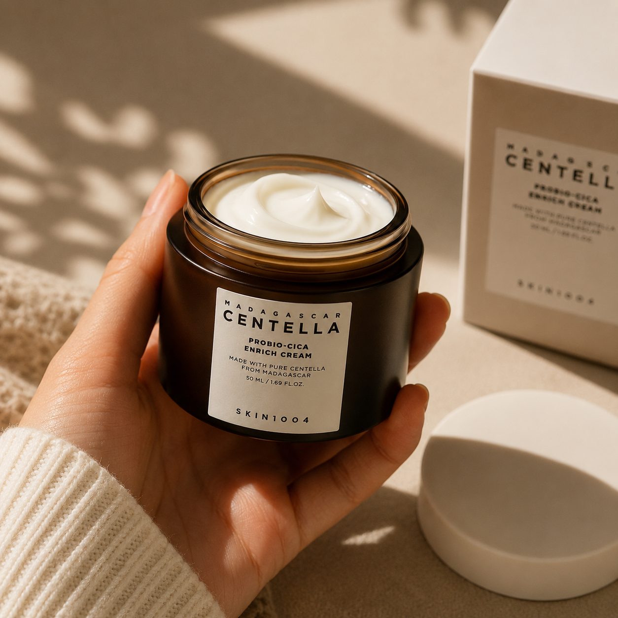 A hand lifting the cream from the open jar
